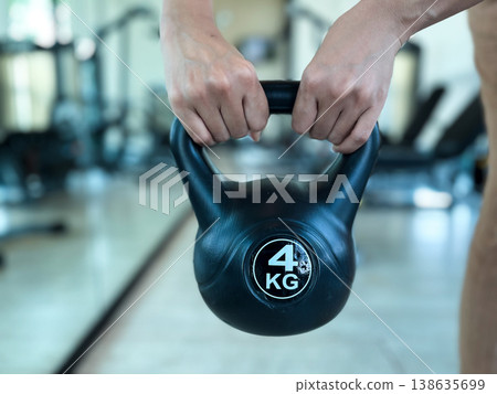 a person holding a 4 kg black kettlebell in a gym. High quality photography showing strength training, fitness workout, bodybuilding, weightlifting, and healthy lifestyle concept 138635699