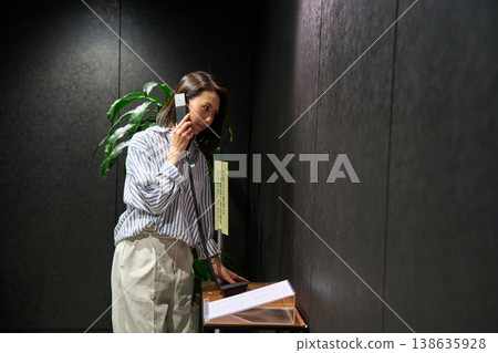 A businesswoman using the receptionist's internal phone at the office entrance. 138635928