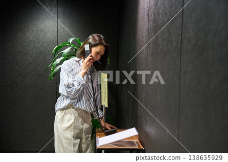 A businesswoman using the receptionist's internal phone at the office entrance. 138635929