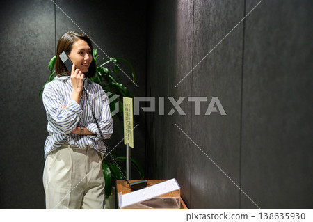 A businesswoman using the receptionist's internal phone at the office entrance. 138635930