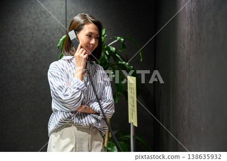 A businesswoman using the receptionist's internal phone at the office entrance. 138635932