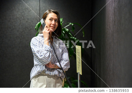 A businesswoman using the receptionist's internal phone at the office entrance. 138635933