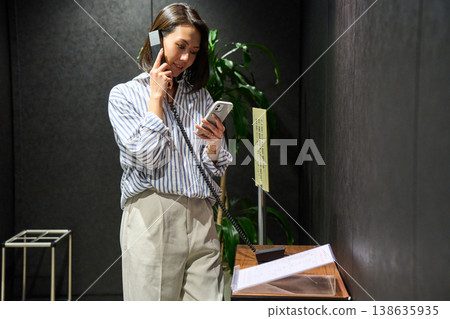 A woman at the office reception desk makes an internal phone call while checking her smartphone. 138635935