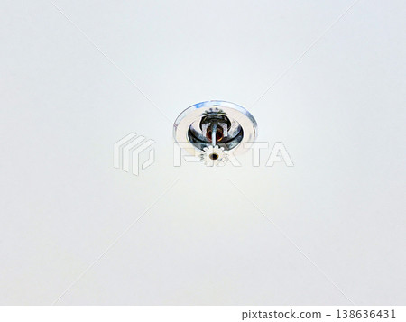 Automatic fire sprinkler head installed on a white ceiling for building safety. High quality photography showing fire protection system, emergency prevention, and indoor security technology 138636431