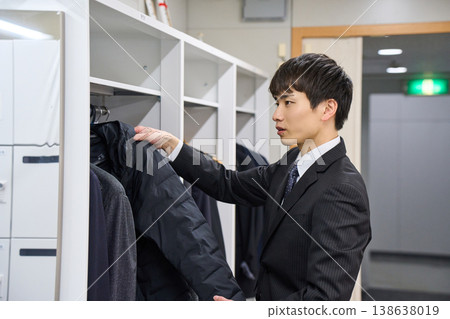 A young businessman hanging his coat in an office locker; a scene of arriving at and leaving work. 138638019