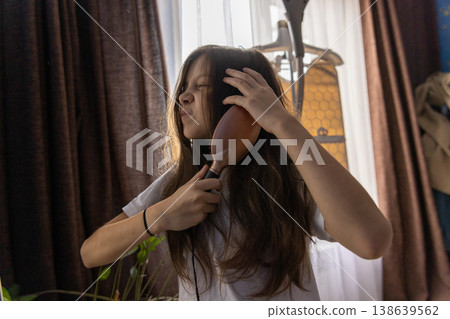 A young girl making a frustrated face while trying to brush her messy long hair in the morning light. A young girl making a frustrated face while trying to brush her messy long hair in the morning light. 138639562