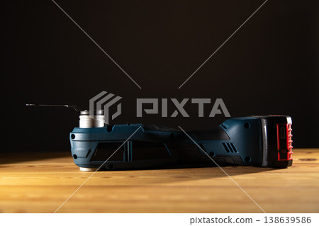 Sleek power tool Multi-cutter showcased on a wooden surface against a dark backdrop, emphasizing its design and functionality, copy space 138639586