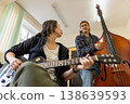 A female guitarist and a male double bass player looking at each other while discussing a song in a college music room. 138639593