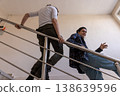 A young man and woman chatting and laughing while leaning on the railings of a university staircase. 138639596