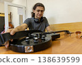 Detailed shot of a music college student carefully replacing old strings on his black electric guitar during a break between classes. 138639599