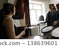 A young female music student with drumsticks looking at her male colleague during a practice session in a studio. 138639601