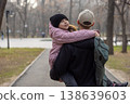 A father walks through a park carrying his daughter in a pink coat, who is hugging him from behind and smiling. 138639603