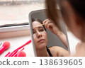 Young female student applying makeup concealer on her forehead and under eyes using an applicator. 138639605
