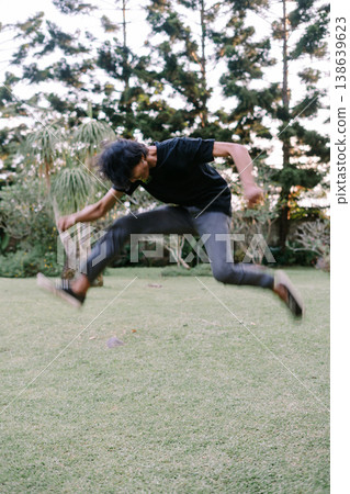 Energetic young man leaps gracefully across green lawn 138639623