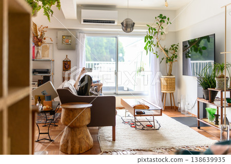 A person looking at their smartphone in a bright living room with houseplants. A person looking at their smartphone in a bright living room with houseplants. 138639935