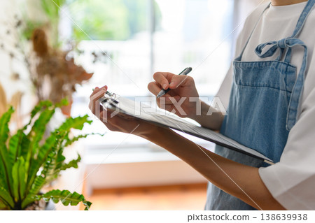 A store clerk wearing an apron takes notes. A store clerk wearing an apron takes notes. 138639938
