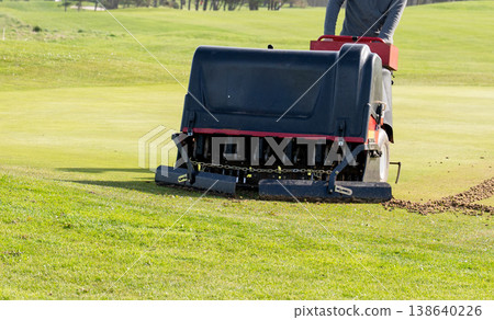 Groundskeeper aerating golf course green with professional turf maintenance machine on sunny day sports field care concept Groundskeeper aerating golf course green with professional turf maintenance machine on sunny day sports field care concept 138640226
