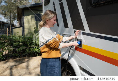 Woman connecting power cable to motorhome campervan at campsite electric hookup travel lifestyle concept Woman connecting power cable to motorhome campervan at campsite electric hookup travel lifestyle concept 138640239