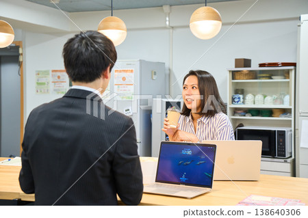 A smiling businesswoman happily chatting with a male colleague in the office break room. A smiling businesswoman happily chatting with a male colleague in the office break room. 138640306