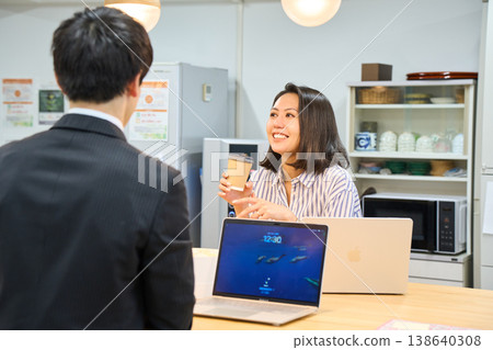 A smiling businesswoman happily chatting with a male colleague in the office break room. 138640308