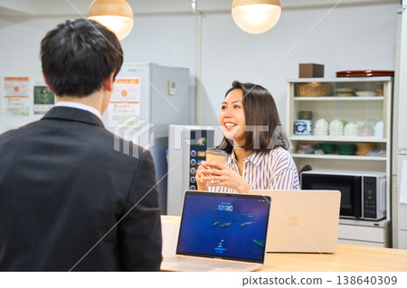 A smiling businesswoman happily chatting with a male colleague in the office break room. A smiling businesswoman happily chatting with a male colleague in the office break room. 138640309