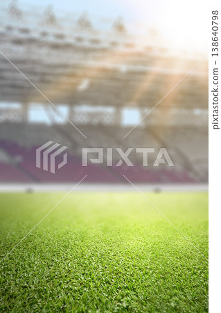 Close-up of lush green grass on a professional soccer field with a blurred stadium and bright sunlight in the background. Ideal for sport-themed designs Close-up of lush green grass on a professional soccer field with a blurred stadium and bright sunlight in the background. Ideal for sport-themed designs 138640798