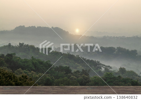A peaceful morning landscape featuring layers of misty green hills and a dense forest under a soft, hazy sunrise A peaceful morning landscape featuring layers of misty green hills and a dense forest under a soft, hazy sunrise 138640832