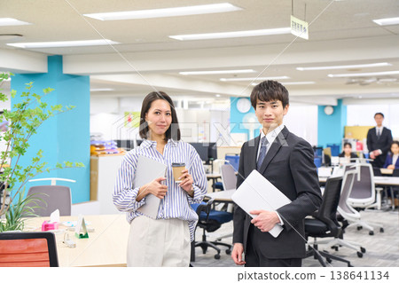 一群面帶笑容的商務人士，男女老少，手持筆記型電腦，在燈光明亮的辦公室裡排成一排。 138641134