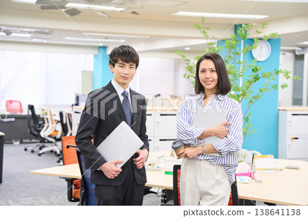 一群面帶笑容的商務人士，男女老少，手持筆記型電腦，在燈光明亮的辦公室裡排成一排。 138641138