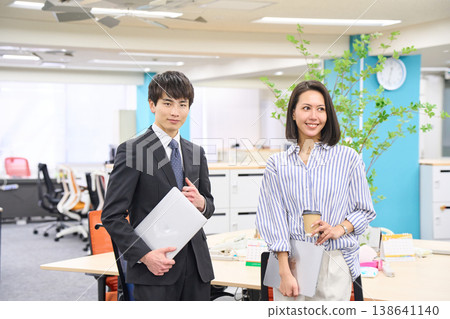 Business professionals, men and women, lined up with smiles on their faces, holding laptops in a brightly lit office. 138641140