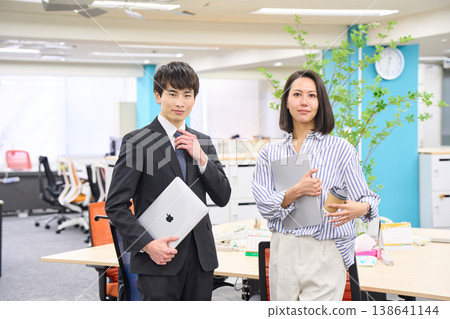 Business professionals, men and women, lined up with smiles on their faces, holding laptops in a brightly lit office. Business professionals, men and women, lined up with smiles on their faces, holding laptops in a brightly lit office. 138641144