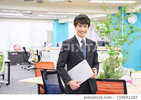A young businessman with a laptop in the office, sporting a cheerful smile. A young businessman with a laptop in the office, sporting a cheerful smile. 138641287