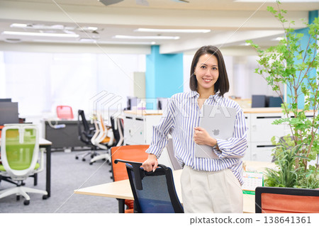 A businesswoman stands with a laptop in her hand, smiling. A businesswoman stands with a laptop in her hand, smiling. 138641361