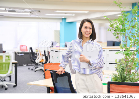 A businesswoman stands with a laptop in her hand, smiling. A businesswoman stands with a laptop in her hand, smiling. 138641363