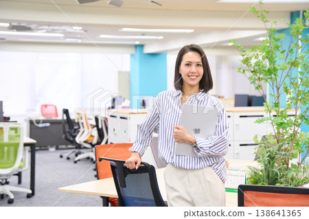 A businesswoman stands with a laptop in her hand, smiling. A businesswoman stands with a laptop in her hand, smiling. 138641365