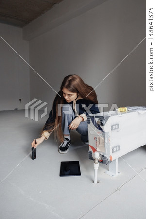 Female interior designer measuring wall with yellow tape measure in a minimalist empty room during renovation. 138641375