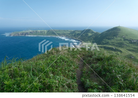 A landscape of green hills overlooking the coast of a remote island; the blue sea and walking paths that stretch across Hokkaido in summer. A landscape of green hills overlooking the coast of a remote island; the blue sea and walking paths that stretch across Hokkaido in summer. 138641554