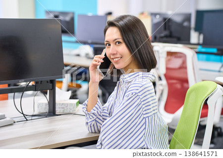 一名女員工在辦公桌前以智慧型手機通話時的側臉特寫。 一名女員工在辦公桌前以智慧型手機通話時的側臉特寫。 138641571