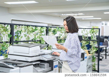一位女商人正在查看辦公室多功能印表機列印的文件。 一位女商人正在查看辦公室多功能印表機列印的文件。 138641594
