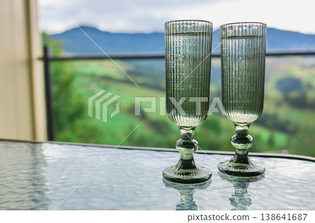 Two green glasses stand on a table with a view of hills and a cloudy sky in the background during a quiet afternoon Two green glasses stand on a table with a view of hills and a cloudy sky in the background during a quiet afternoon 138641687