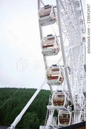 Large ferris wheel stands above green trees on a clear day during daytime in an amusement park setting 138641697