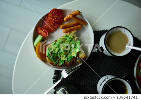 Enjoying avocado toast with coffee and sides at a cozy cafe in the morning light Enjoying avocado toast with coffee and sides at a cozy cafe in the morning light 138641741