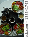 Breakfast spread featuring avocado toast, coffee, and sides on a round table in the morning light 138641743