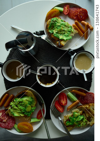 Breakfast spread featuring avocado toast, coffee, and sides on a round table in the morning light Breakfast spread featuring avocado toast, coffee, and sides on a round table in the morning light 138641743