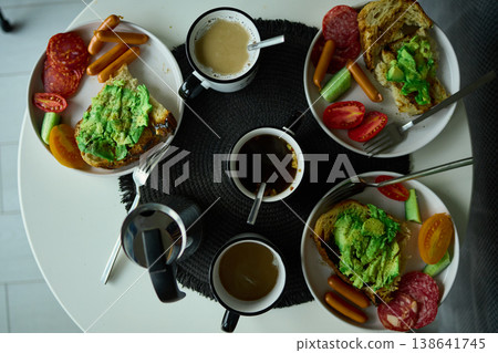 Breakfast spread featuring avocado toast, coffee, and sides on a round table in the morning light Breakfast spread featuring avocado toast, coffee, and sides on a round table in the morning light 138641745