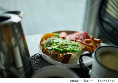 Enjoying avocado toast with coffee and sides at a cozy cafe in the morning light Enjoying avocado toast with coffee and sides at a cozy cafe in the morning light 138641748