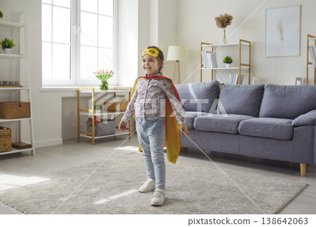 Little girl in yellow mask and cape playing superhero in living room at home 138642063