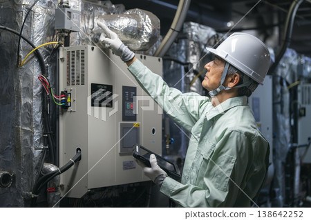 A profile view of a worker inspecting the building's air conditioning system (absorption chiller/heater). Building maintenance staff. (Image) 138642252