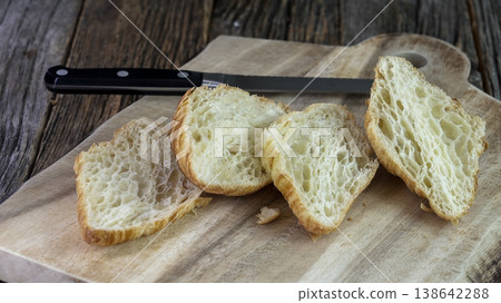 Four slices of crusty bread sit on a wooden cutting board with a knife nearby Four slices of crusty bread sit on a wooden cutting board with a knife nearby 138642288