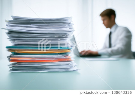 Person handling pressing documents next to a laptop. Busy office worker typing on keyboard beside towering pile of paperwork on desk. Stressed professional man working under pressure amidst deadline Person handling pressing documents next to a laptop. Busy office worker typing on keyboard beside towering pile of paperwork on desk. Stressed professional man working under pressure amidst deadline 138643336
